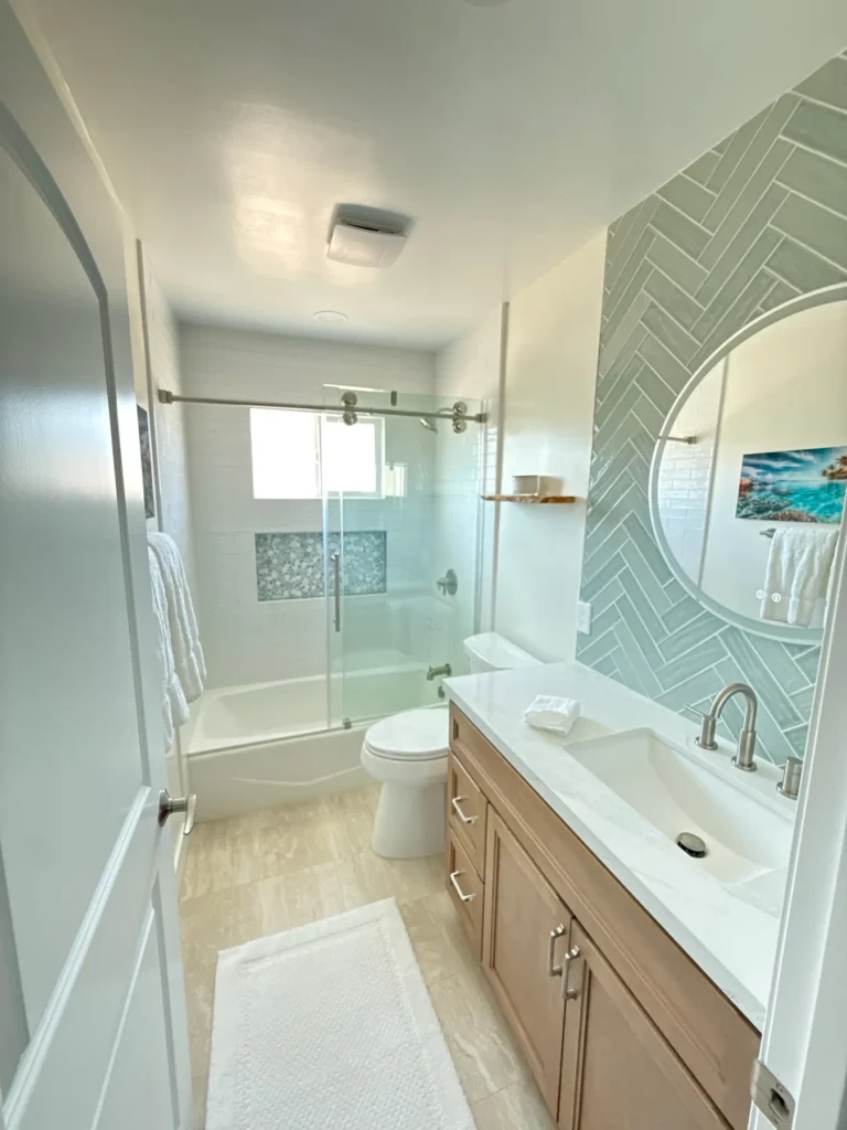 Guest bath with green herringbone tile, a wood vanity and a glass tub enclosure