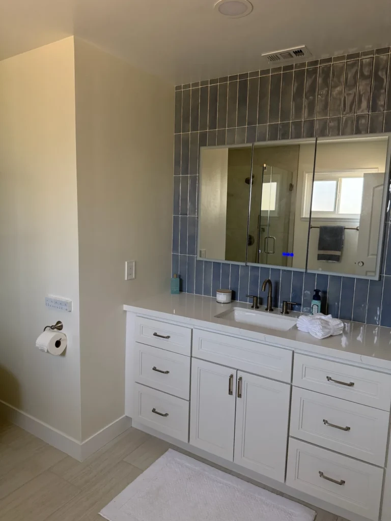 Primary bath with a blue tile feature wall, white shaker vanity and wide mirror