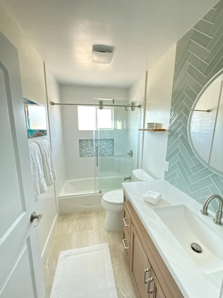 Long view of the green herringbone tile bath with a wood vanity