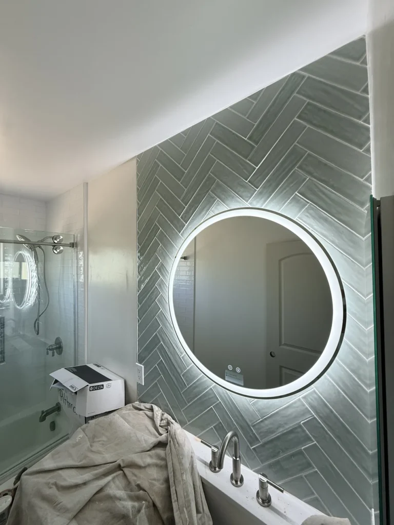 Backlit round mirror on green herringbone tile
