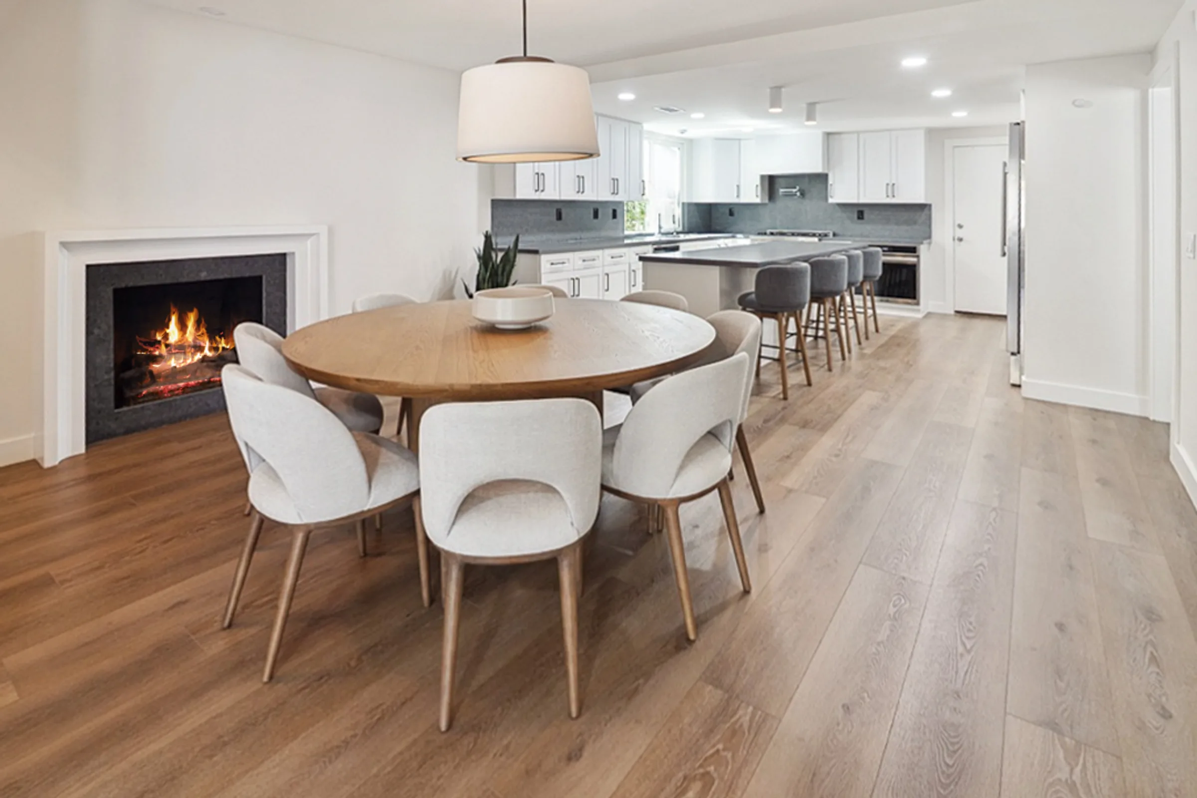 Open dining area and kitchen remodeled by Casa Renovations, with a lit fireplace and wide plank flooring