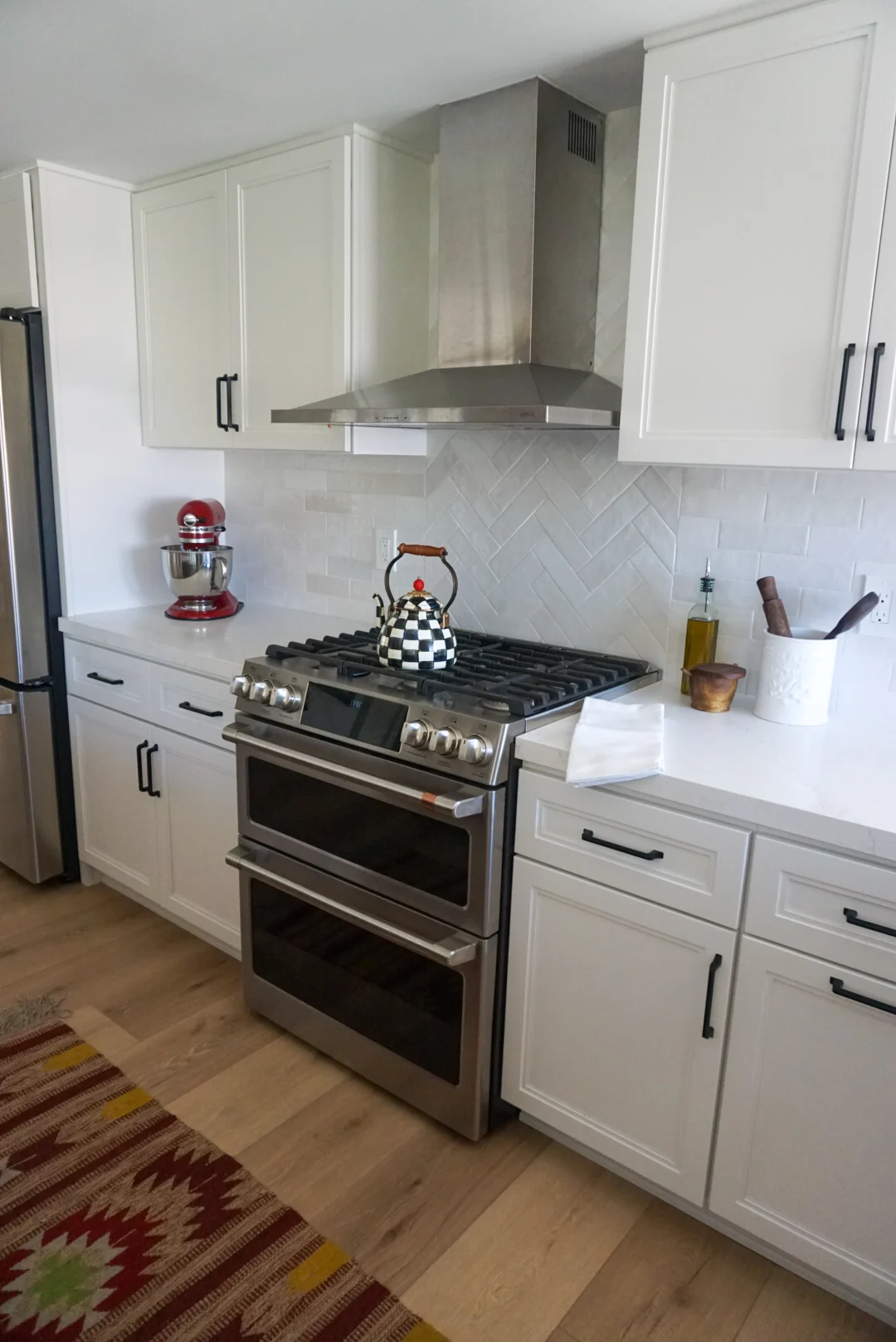 White kitchen with a herringbone tile backsplash, stainless range and double oven